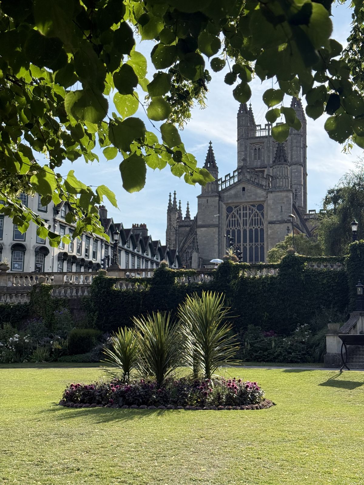 Bath Abbey's tower rising beyond the trees and flowerbeds of Parade Gardens